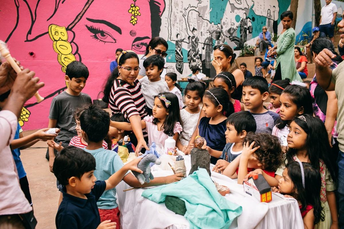 Children gathered around a puppet-making table in front of a pink mural