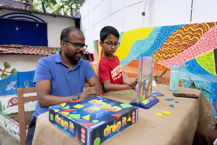 A volunteer playing a board game with a boy beside a mural
