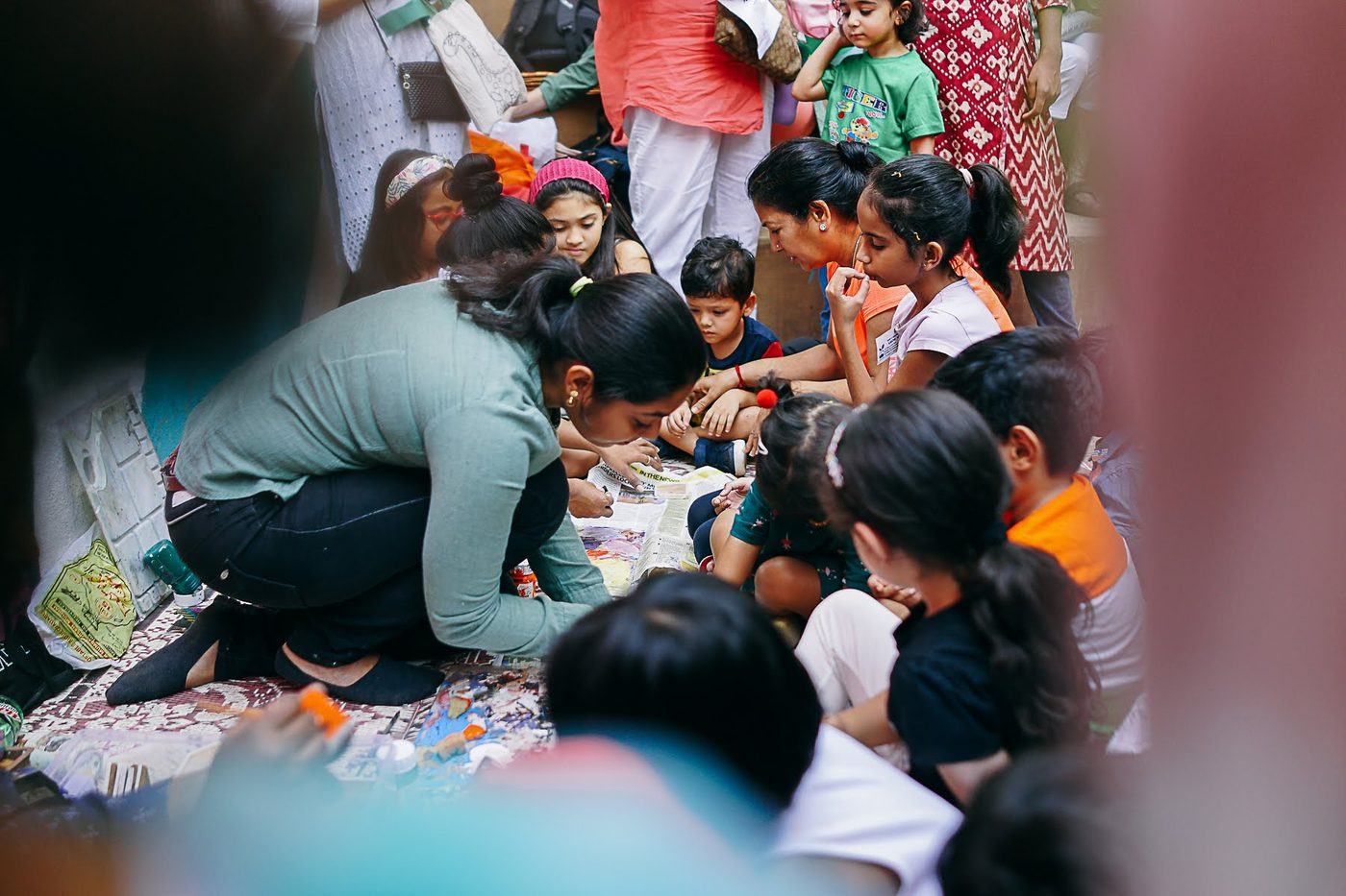 A facilitator kneeling among children at a crowded craft workshop table