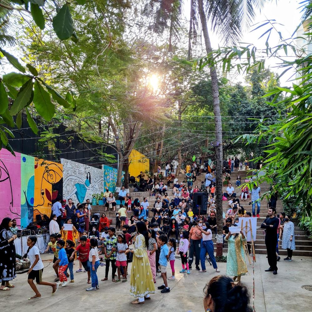 Families and children on the landing in the late afternoon sun, with murals and trees behind